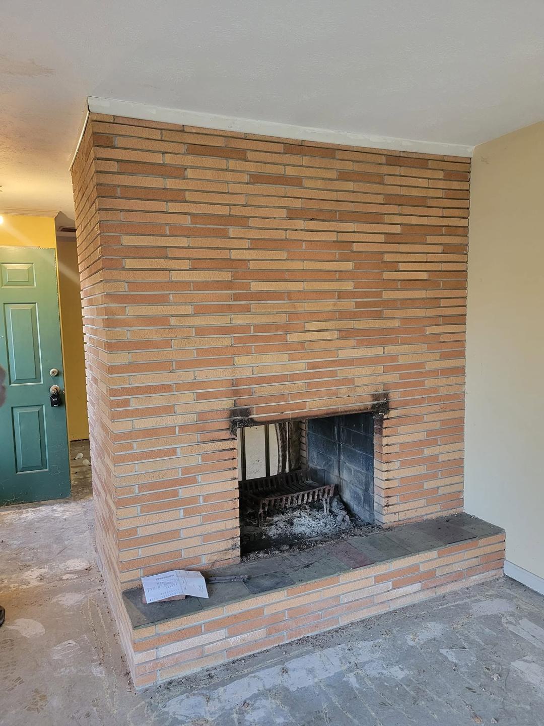 Fireplace Removal Before Before fireplace removal: brick indoor fireplace with firebox, hearth, and ash in yellow-walled room.