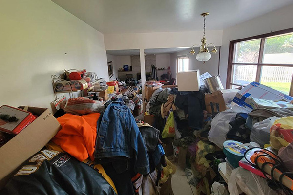 Before hoarder cleanup: room overflowing with piled clothes, boxes, toys, and household junk.